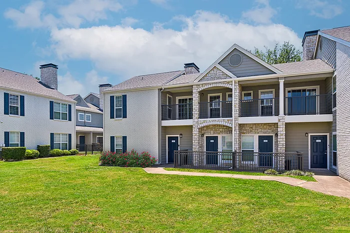 Charming apartment community with modern two-story buildings, stone facade, and inviting balconies set in a lush green landscape.
