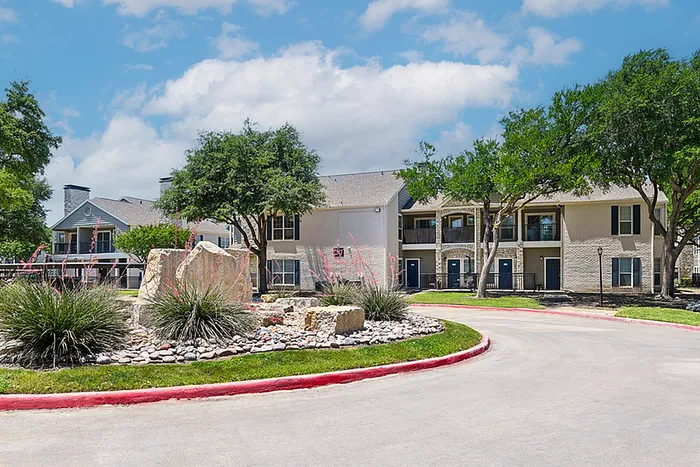 Charming apartment community with beautifully landscaped gardens, mature trees, and inviting pathways under a sunny sky.