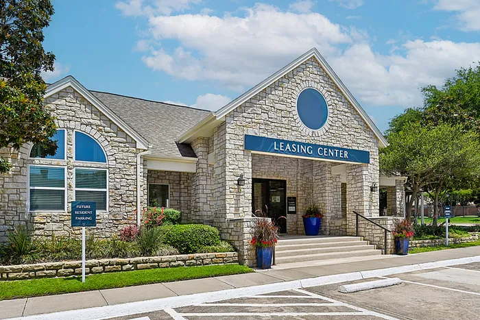 Inviting leasing center with charming stone facade, set amidst lush greenery and bright blue planters.