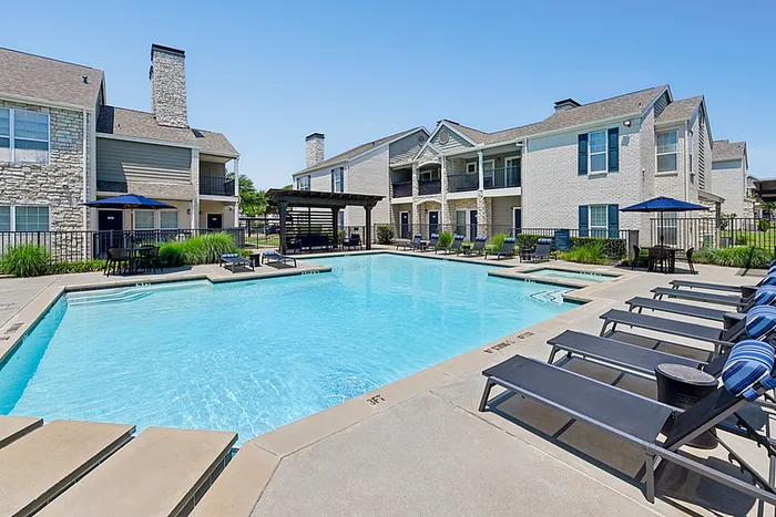Inviting apartment community with a swimming pool, elegant architecture, and relaxing lounge chairs, perfect for luxurious living.