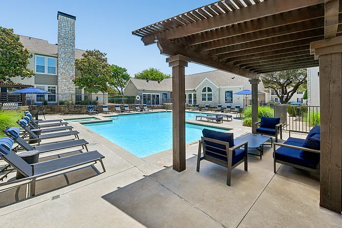Inviting outdoor pool area with comfortable lounge seating and stylish pergola, surrounded by lush greenery and elegant architecture.