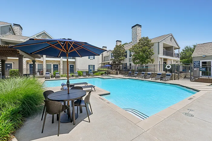 Inviting apartment community with a swimming pool, surrounded by stylish lounge chairs and a chic outdoor dining area with umbrella.