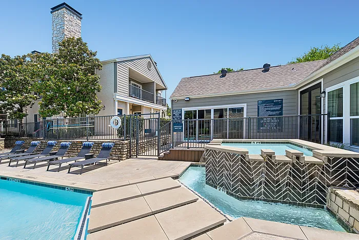 Charming apartment community featuring a refreshing pool, elegant stone architecture, and inviting sun loungers under a clear blue sky.