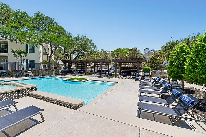 Inviting outdoor pool area with sun loungers, lush greenery, and elegant pergolas in a serene apartment complex.