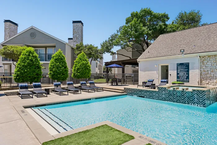 Inviting outdoor swimming pool area with stylish lounge chairs and beautiful trees, perfect for relaxation and enjoyment in a scenic apartment setting.