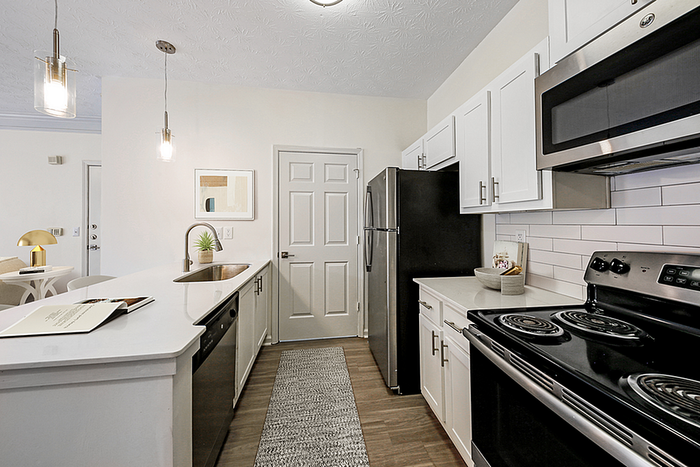 Modern kitchen with sleek stainless steel appliances, white cabinetry, and elegant pendant lighting.