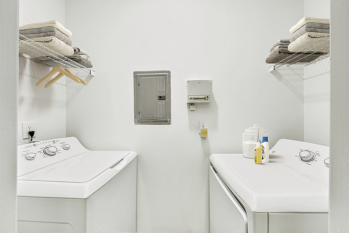 Bright and functional laundry room featuring modern washer and dryer, stylish shelving, and neatly organized linens.