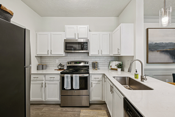 Modern kitchen with sleek stainless steel appliances, white cabinetry, and elegant countertop featuring a stylish backsplash and ambient lighting.
