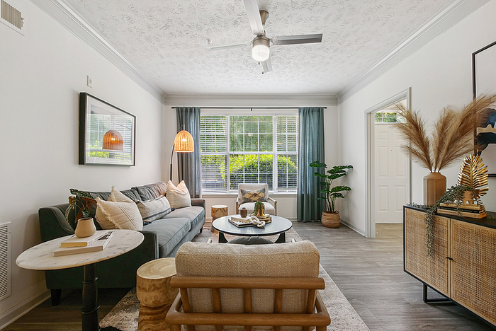 Bright and inviting living room featuring modern decor, a comfortable sofa, stylish lighting, and large windows with lush green views.
