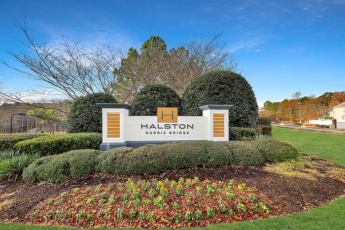 Elegant entrance sign for Halston Harris Bridge surrounded by lush greenery and vibrant landscaping under a clear blue sky.