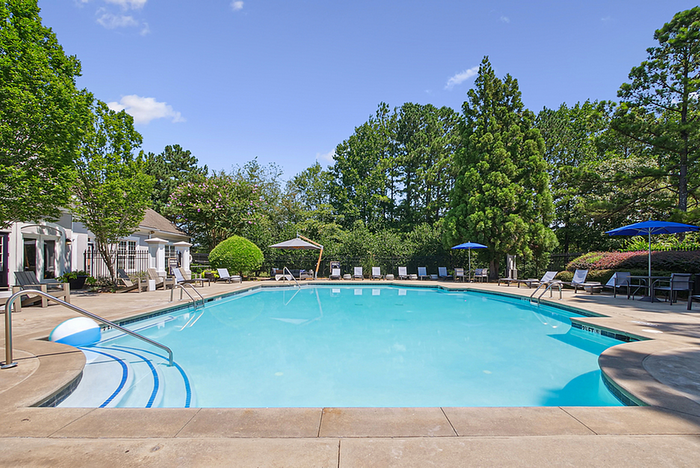 Inviting outdoor pool area surrounded by lush greenery, sun loungers, and vibrant blue umbrellas.