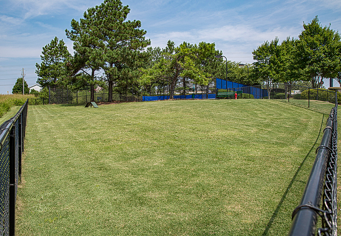 Expansive fenced dog park with lush green grass and mature trees, perfect for pet-friendly living.