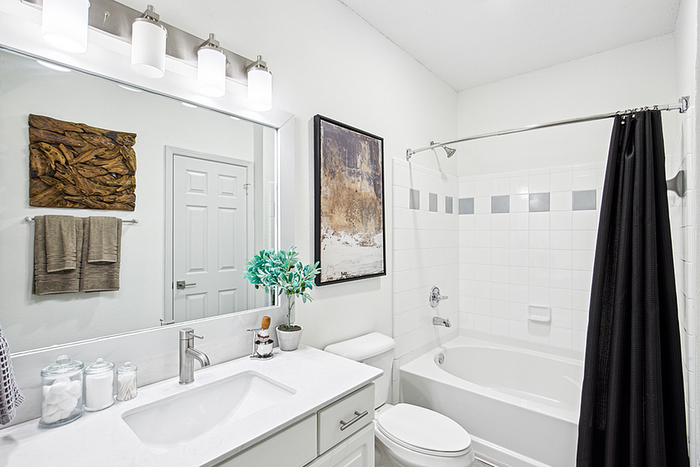 Modern bathroom with elegant white tiles, inviting tub, sleek vanity with a large mirror, and artistic wall decor.