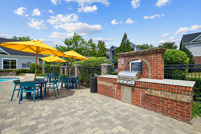 Inviting outdoor patio area with vibrant yellow umbrellas, modern seating, and a built-in brick barbecue grill, ideal for relaxation and entertaining.
