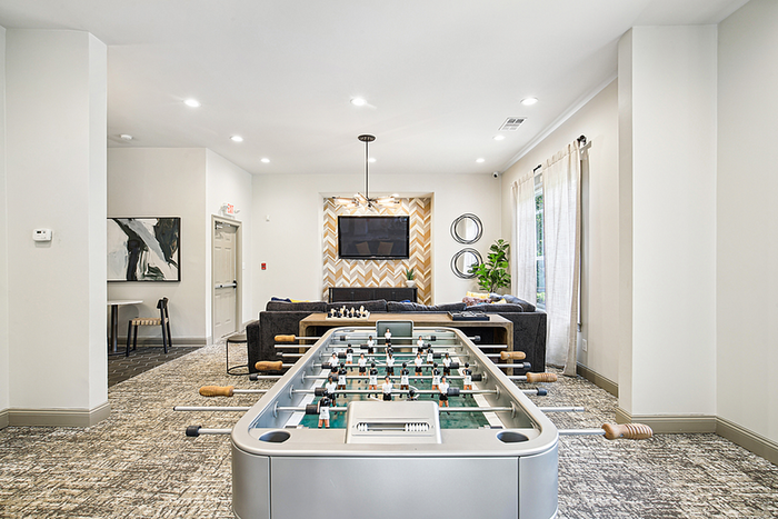 Inviting recreational room with elegant foosball table, plush seating, modern decor, and abundant natural light.