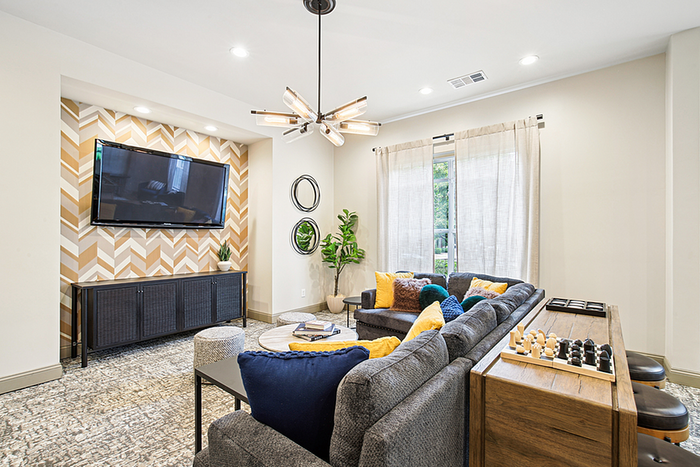 Contemporary living room featuring a cozy gray sectional, vibrant yellow and blue cushions, stylish geometric accent wall, and modern lighting.