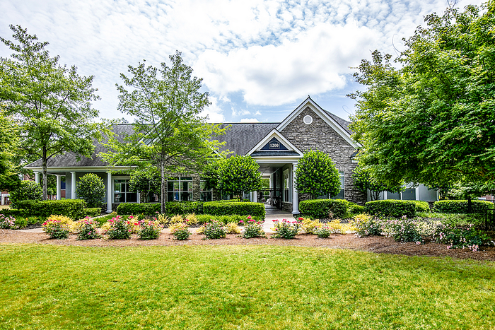Charming residential building surrounded by lush greenery and colorful gardens under a bright blue sky.