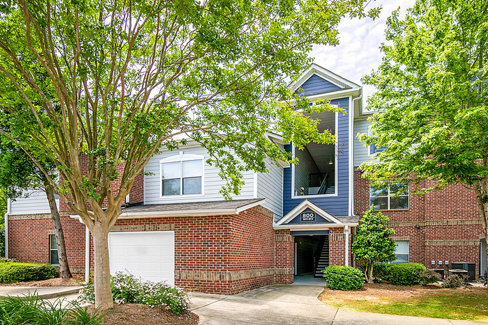 Charming brick townhouse with lush green landscaping and a welcoming entrance, ideal for modern living.