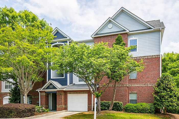Charming suburban townhouse with vibrant landscaping, featuring red brick facade and multi-level architectural design.