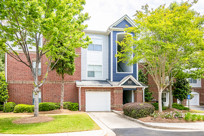 Charming red brick apartment building with lush greenery and a welcoming entrance, offering modern comfort in a serene setting.
