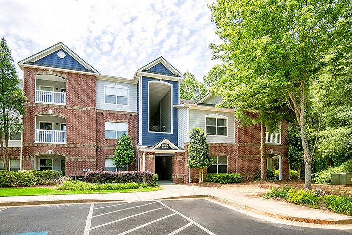 Charming brick apartment complex with white railings, nestled in lush greenery on a sunny day.