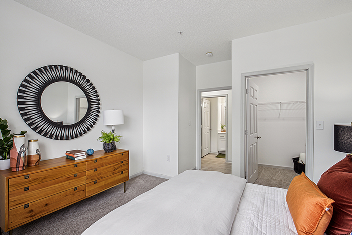 Elegant bedroom with a stylish wooden dresser, decorative mirror, and spacious walk-in closet, exuding modern charm and comfort.