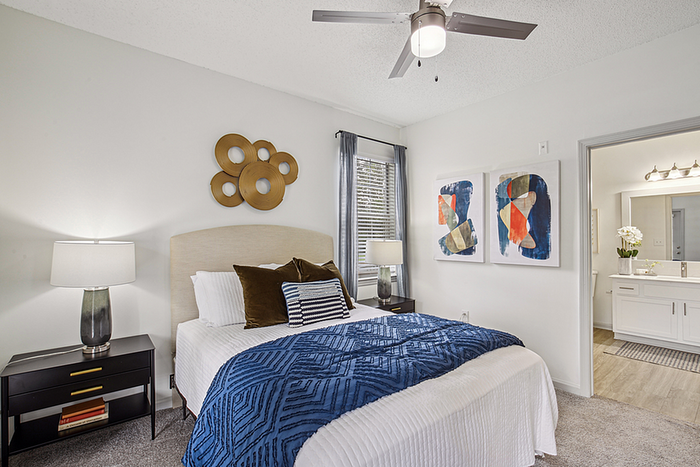 Elegant bedroom with modern decor, featuring a cozy bed with rich blue accents, stylish artwork, and an adjoining chic bathroom.