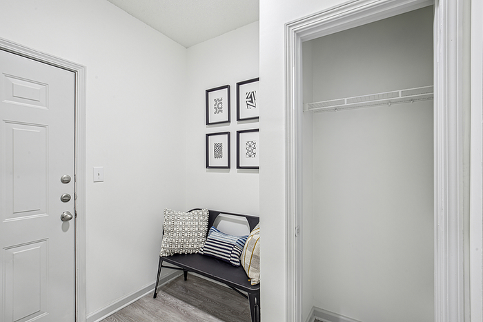 Inviting apartment entrance with modern decor, featuring a cozy bench with stylish cushions and framed artwork on pristine white walls.