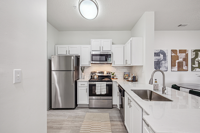 Modern kitchen with sleek white cabinetry, stainless steel appliances, and stylish lighting. Open concept with a chic dining area featuring contemporary artwork.