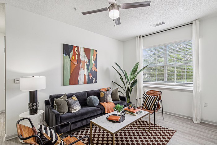 Bright and modern living room with chic decor, featuring a cozy sofa, stylish armchairs, and vibrant artwork, filled with natural light from large windows.