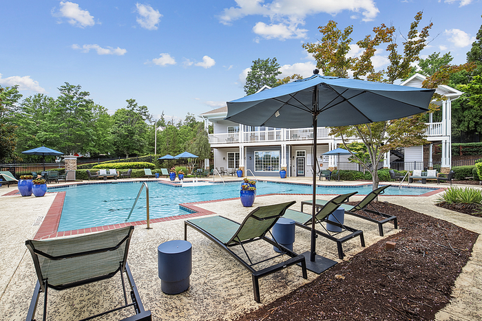 Charming outdoor pool area with comfortable lounge chairs, vibrant blue umbrellas, and lush green surroundings, perfect for relaxation.