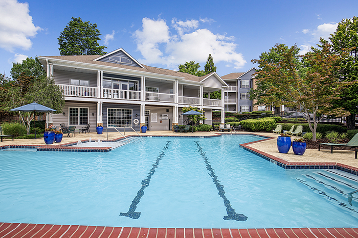 Inviting swimming pool area with modern lounge chairs and vibrant landscaping, set against a charming two-story clubhouse with balcony.