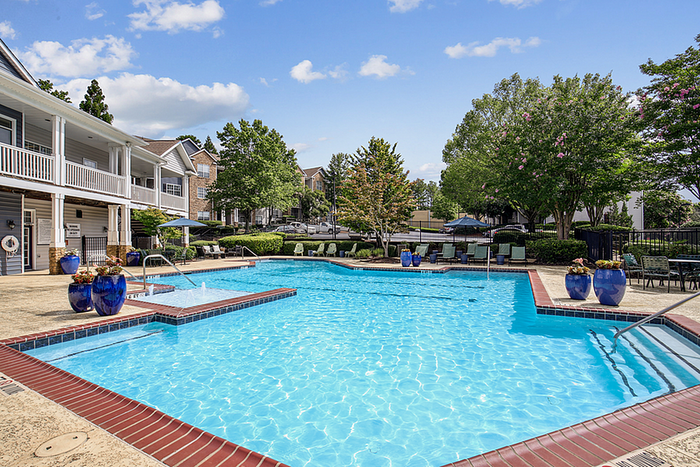 Inviting outdoor pool area with modern lounge seating, surrounded by lush greenery and elegant blue planters, perfect for relaxation and enjoyment.