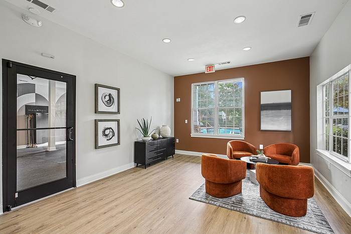 Inviting modern lounge area with vibrant orange chairs, elegant art, and abundant sunlight from large windows.