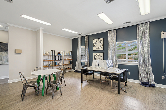 Elegant cyber cafe and media lounge with modern decor, featuring a sleek desk setup with computers, a stylish round table with metal chairs, and large windows with natural light.