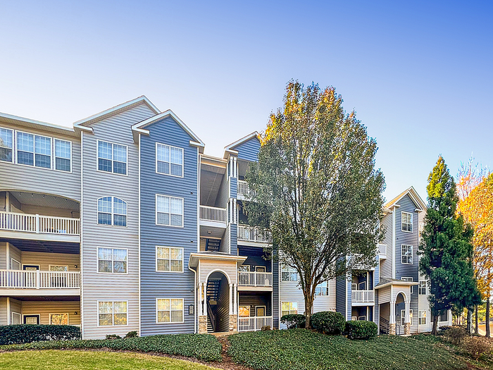 Charming multi-story apartment community surrounded by lush greenery and vibrant trees under a clear blue sky.