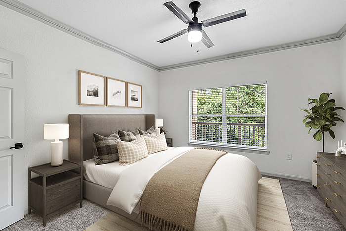 Inviting bedroom with cozy bedding and large window offering serene green views, accented by modern decor and soft lighting.