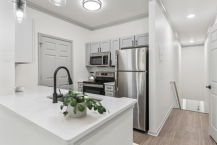 Modern kitchen with sleek stainless steel appliances, elegant white countertops, and a stylish black faucet. Contemporary lighting complements the cozy yet sophisticated space.