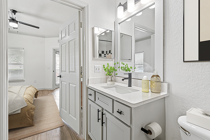Bright and modern bathroom adjacent to a cozy bedroom, featuring sleek white cabinets, elegant lighting, and stylish decor.