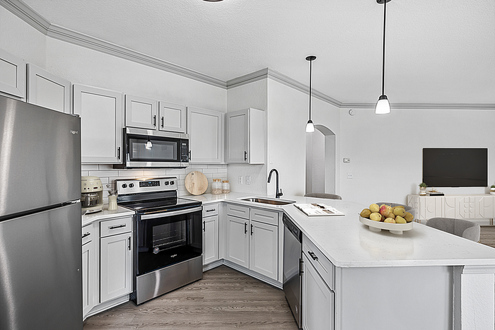 Modern kitchen with sleek stainless steel appliances, white cabinetry, and elegant pendant lighting, opening into a bright living area.