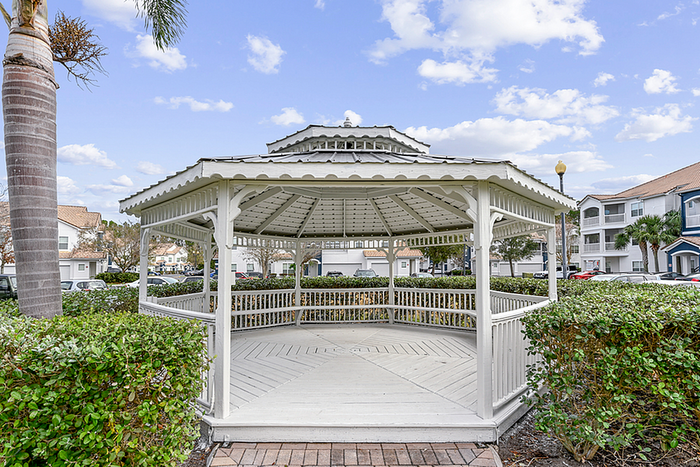 Charming white gazebo nestled amidst lush greenery, perfect for relaxing in scenic community surroundings.
