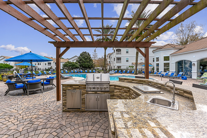 Luxurious outdoor area with a sparkling pool, modern grill station, and stylish seating under a wooden pergola, perfect for entertaining.