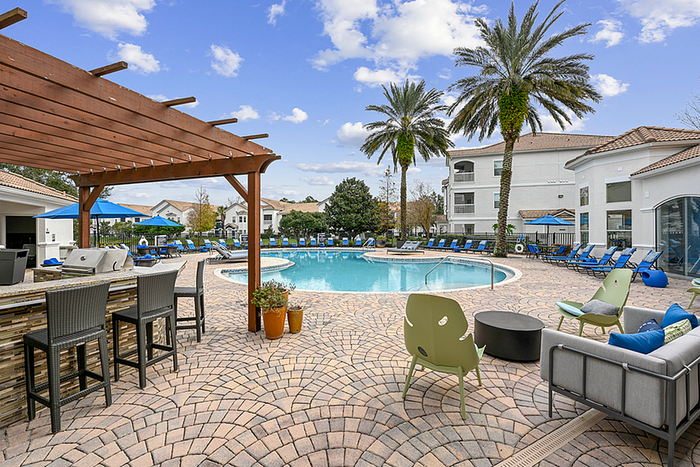 Elegant apartment community featuring a stunning pool area with palm trees, stylish outdoor seating, and a cozy BBQ setup under a wooden pergola.