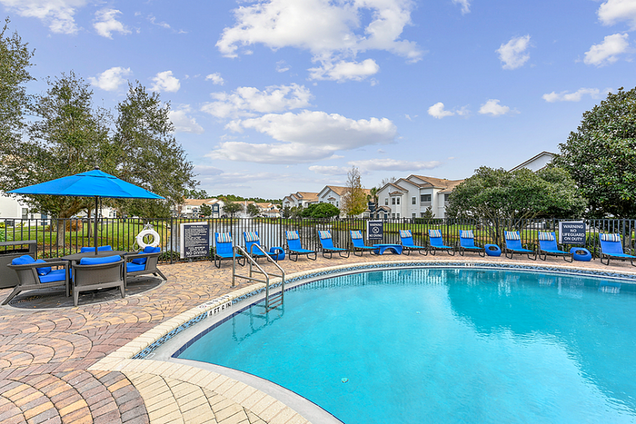 Inviting outdoor pool area with comfortable lounge seating and bright blue parasols, surrounded by lush greenery and picturesque residential views.