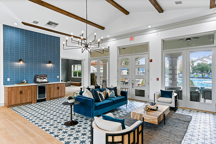 Elegant contemporary clubhouse lounge with plush blue furnishings, stylish chandelier, and large windows offering scenic pool views.