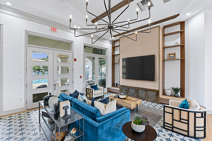 Chicclubhouse with stylish blue sofa, elegant chandelier, and pool view through large windows.