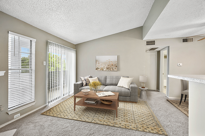 Bright and inviting living room with a cozy gray sofa, stylish coffee table, and large windows framing outdoor greenery, perfect for relaxing.