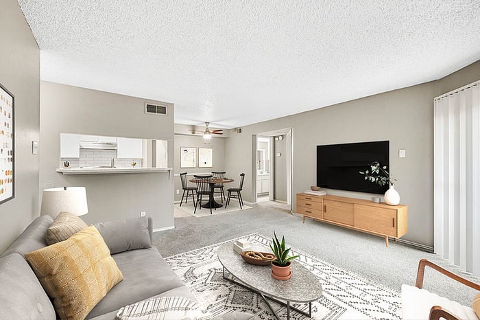 Modern and spacious living room with a cozy gray sofa, stylish decor, and a sleek entertainment center, leading to a bright dining area and kitchen.