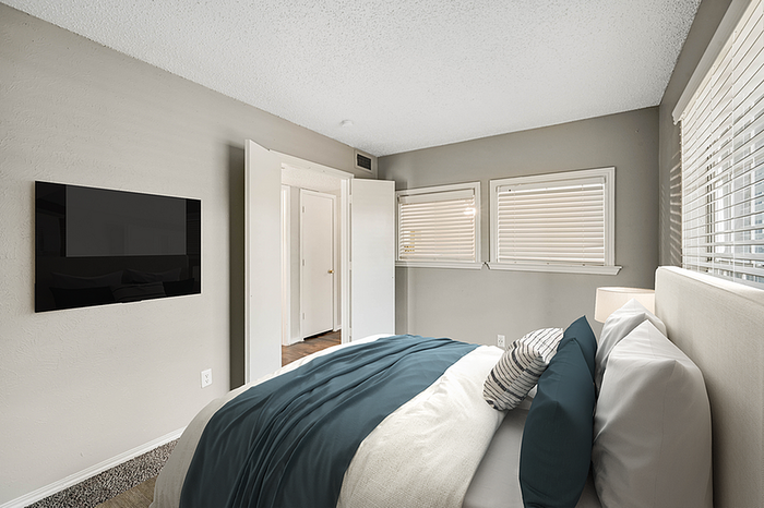 Inviting bedroom with modern decor, featuring a cozy bed, sleek wall-mounted TV, and ample natural light from double windows.