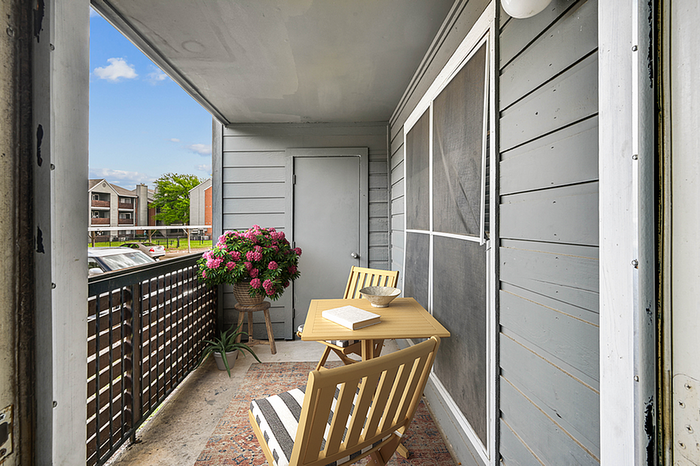 Charming apartment balcony with cozy seating, table for two, vibrant flowers, and a serene view of surrounding residential area.